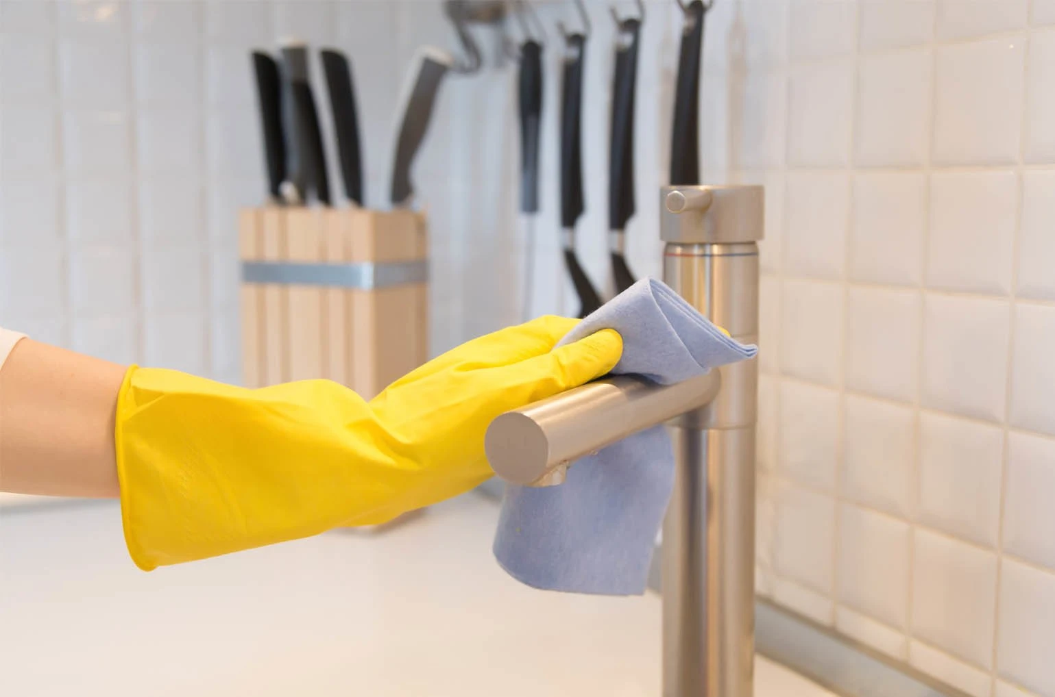 female hand cleaning a kitchen faucet with products that make kitchen cleaning easy