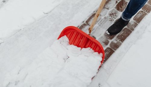 red snow shovel pushing snow to reveal brick sidewalk